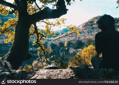 A girl with her back sitting under the shade of a tree enjoying the landscape relaxed