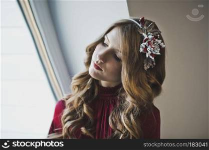 A girl with long brown hair by the window.. Portrait of a girl in a red dress at the window 4425.
