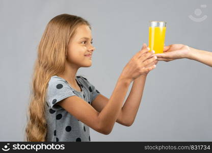 A girl with two hands takes a glass of juice from the hand of another person