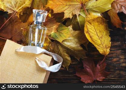 A glass bottle of female perfume with gift bag laid on autumn yellow leaves on a wooden background. Natural perfumery. Autumn season.. A glass bottle of female perfume with gift bag laid on autumn yellow leaves on a wooden background. Natural perfumery.