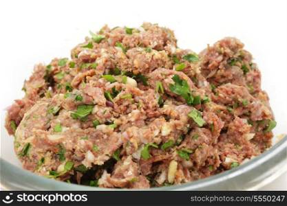 A glass bowl full of a mixture of minced beef, onion and breadcrumbs, with chopped parsley, garlic and spices ready for forming into homemade beefburgers.