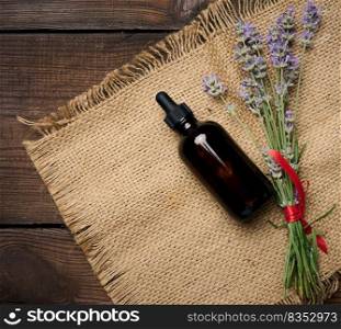 A glass brown bottle with a pipette and a bouquet of lavender on a brown wooden table. Container for cosmetic oils, serum