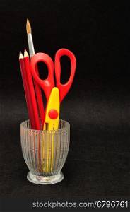 A glass container with scissors and pencils