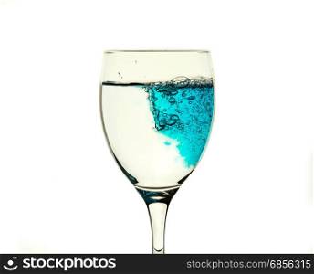 A glass glass with clear water is filled with a blue liquid