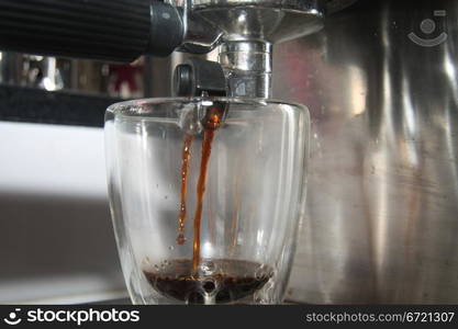 A glass in close up under a traditional italian espresso maker