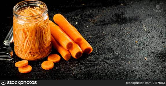 A glass jar with canned carrots. On a black background. High quality photo. A glass jar with canned carrots.