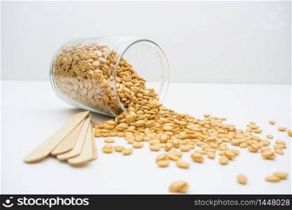 A glass jar with golden wax granules and wooden sticks isolated on a white background.
