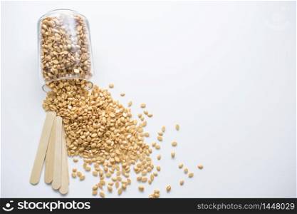 A glass jar with golden wax granules and wooden sticks isolated on a white background.