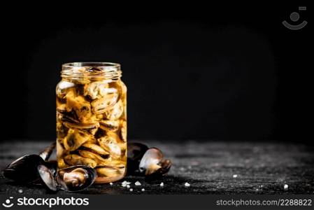 A glass jar with pickled mussels on the table. On a black background. High quality photo. A glass jar with pickled mussels on the table.