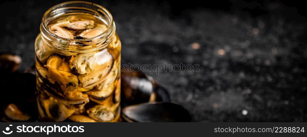 A glass jar with pickled mussels on the table. On a black background. High quality photo. A glass jar with pickled mussels on the table.