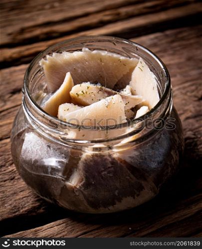 A glass jar with pieces of salted herring. On a wooden background. High quality photo. A glass jar with pieces of salted herring.