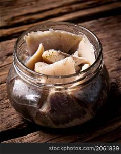 A glass jar with pieces of salted herring. On a wooden background. High quality photo. A glass jar with pieces of salted herring.