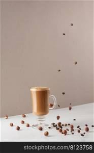 A glass of cappuccino with fragrant foam and falling hazelnuts and roasted coffee beans. Hot latte or cappuccino in a glass cup. Creative design for cafes and restaurants with a cup of coffee. 