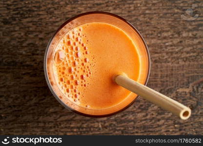 A glass of carrot juice with a bamboo straw, top view