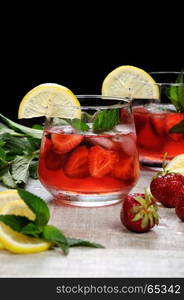 A glass of chilled strawberry lemonade, mint leaves, a slice of lemon with ice