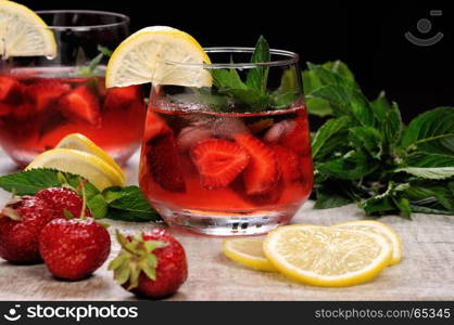 A glass of chilled strawberry lemonade, mint leaves, a slice of lemon with ice