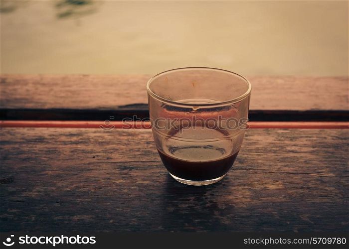 A glass of coffee on a table by a lake in the afternoon