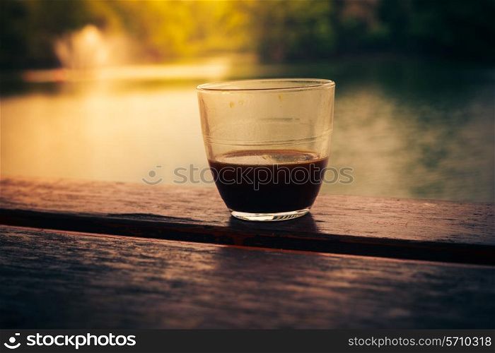 A glass of coffee on a table by a lake in the afternoon