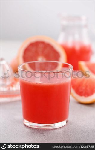 A glass of freshly made grapefruit juice and slices of fresh fruit on a light concrete background. Healthy and diet drink. Close-up