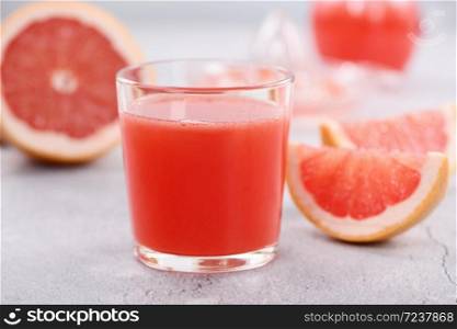 A glass of freshly made grapefruit juice and slices of fresh fruit on a light concrete background. Healthy and diet drink. Close-up
