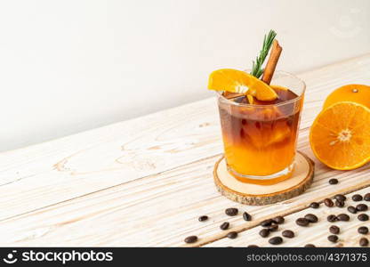 A glass of iced americano black coffee and layer of orange and lemon juice decorated with rosemary and cinnamon on wood background