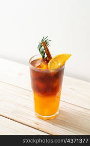 A glass of iced americano black coffee and layer of orange and lemon juice decorated with rosemary and cinnamon on wood background