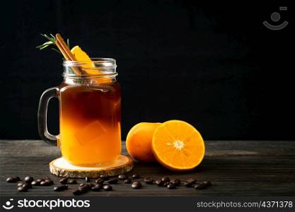 A glass of iced americano black coffee and layer of orange and lemon juice decorated with rosemary and cinnamon