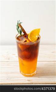 A glass of iced americano black coffee and layer of orange and lemon juice decorated with rosemary and cinnamon on wood background