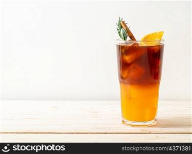 A glass of iced americano black coffee and layer of orange and lemon juice decorated with rosemary and cinnamon on wood background