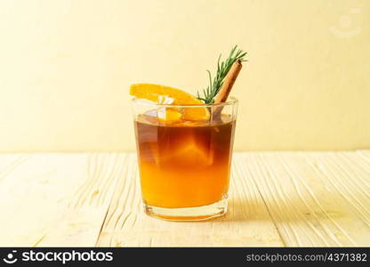 A glass of iced americano black coffee and layer of orange and lemon juice decorated with rosemary and cinnamon