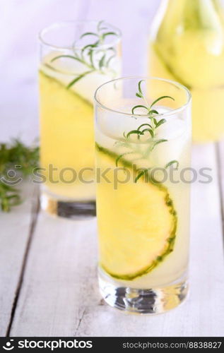 A glass of lemonade with pineapple pieces, ice cubes and rosemary. Cold refreshment organic non-alcohol cocktail.