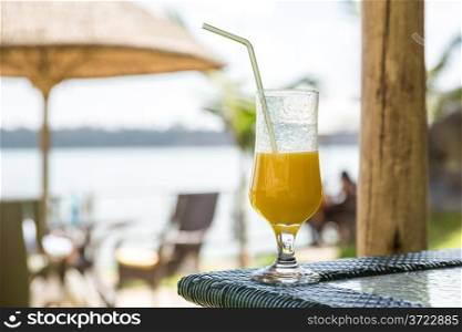 A glass of mango juice with a straw placed on a table at a vacation spot.