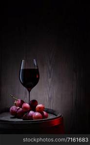 A glass of red wine and a bunch of pink grapes on an old wooden barrel. Glass of red wine and pink grapes on wooden barrel