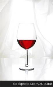 A glass of red wine in Bordeaux-shaped glass on a light background