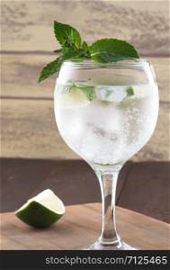 A glass of refreshing lemonade and lime wedges. Cold fresh lemonade drink on a wooden background