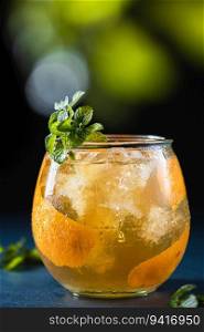A glass of scotch whiskey with orange juice and orange decoration with fresh mint on a dark background