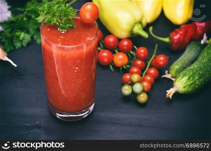 a glass of tomato juice on a black table in the middle of fresh vegetables, vintage toning