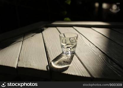 a glass of water on a white table with rays of the sun with nature background. glass of glass with water. a glass of water on a white table with rays of the sun with nature background