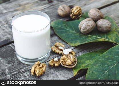 A glass of white milk and walnuts on an old wooden table. Vegan milk from walnuts. Eco food. Keto is drinking.. A glass of white milk and walnuts on an old wooden table. Vegan milk from walnuts. Eco food.