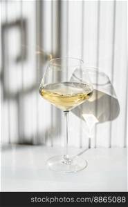A glass of white wine on the white background with geometric shadow effect, modern composition.. A glass of white wine