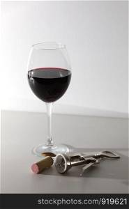 a glass of wine and some wine tools on a white wooden surface. a glass of wine and some wine tools on a white wooden surface. Red wine