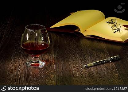 A glass with cognac, cigar and an old book nearby