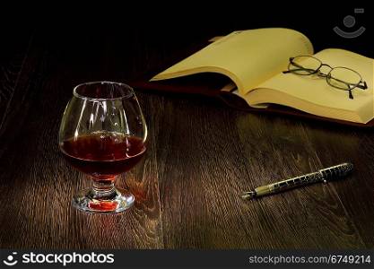 A glass with cognac, cigar and an old book nearby