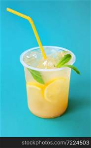 A glass with lemonade or mojito cocktail with lemon and mint, cold refreshing drink or beverage with ice on blue background