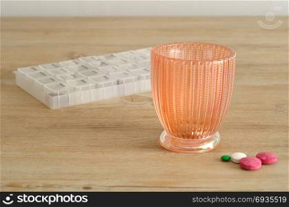 A glass with pills displayed on a wooden background