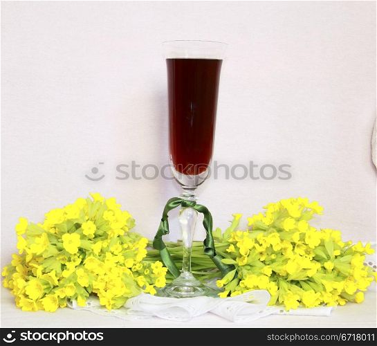 A glass with wine on a lacy napkin and a bouquet yellow field flowers