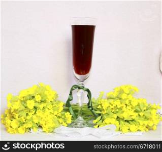 A glass with wine on a lacy napkin and a bouquet yellow field flowers