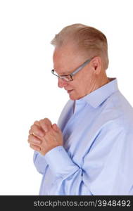 A good looking senior man in a blue shirt and his hands felted standingpraying isolated for white background.