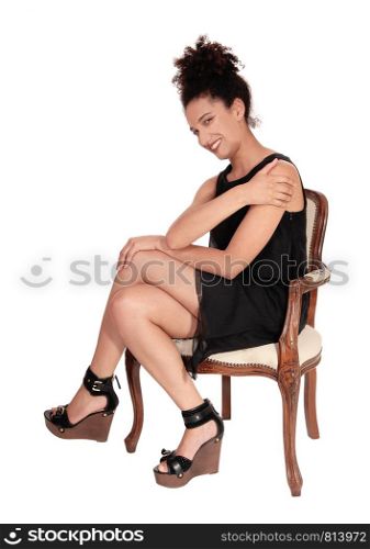 A gorgeous multi-racial woman sitting in a short black dress in an old armchair smiling with her curly black hair in a bun on her head, isolatedfor white background