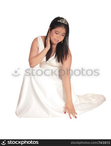 A gorgeous young bride in her white wedding dress crouching on the floor with a crown in her black hair, isolated for white background